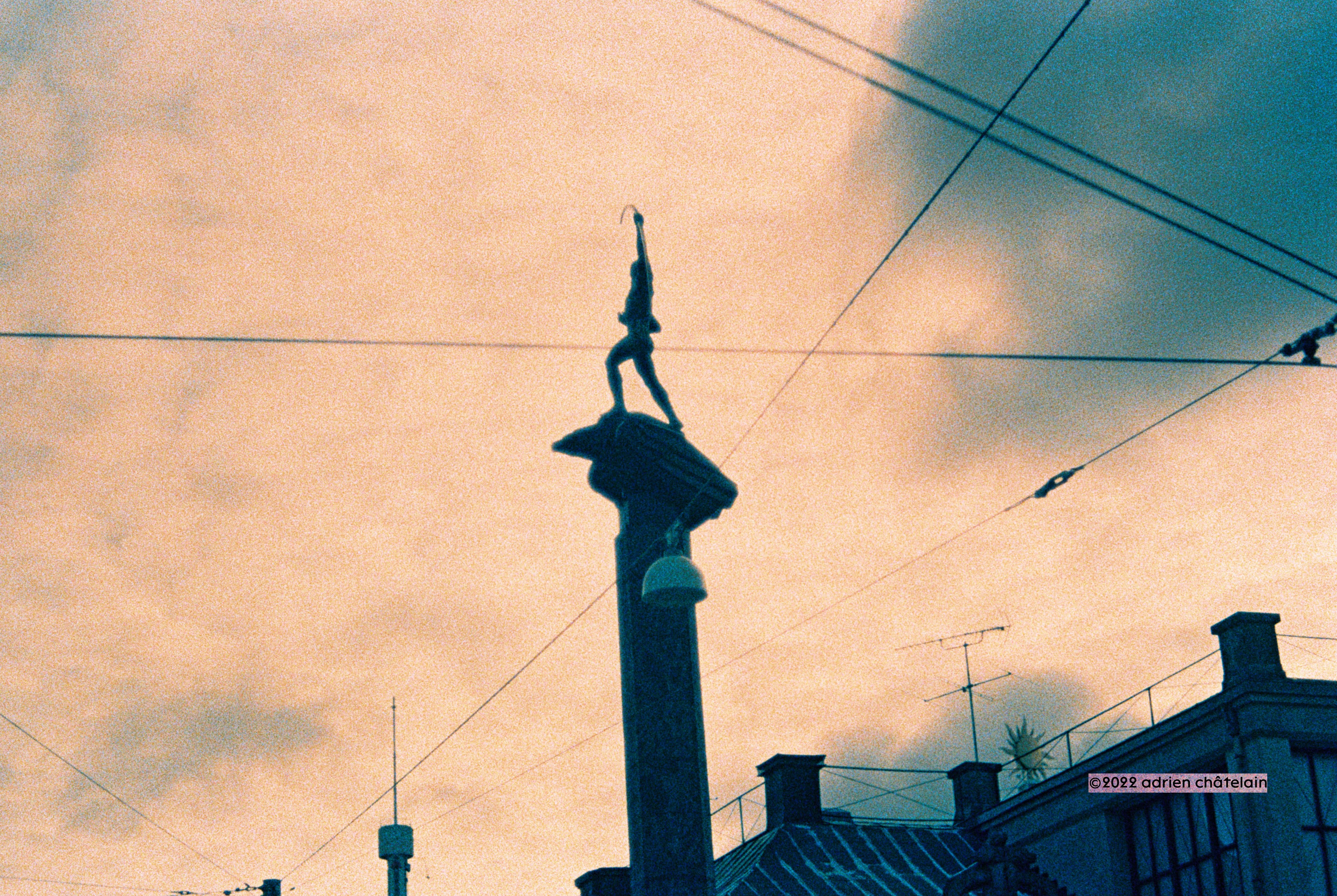 Cross Processed analog photo of Carl Milles' The Archer framed by overhead tram power lines, Stockholm
